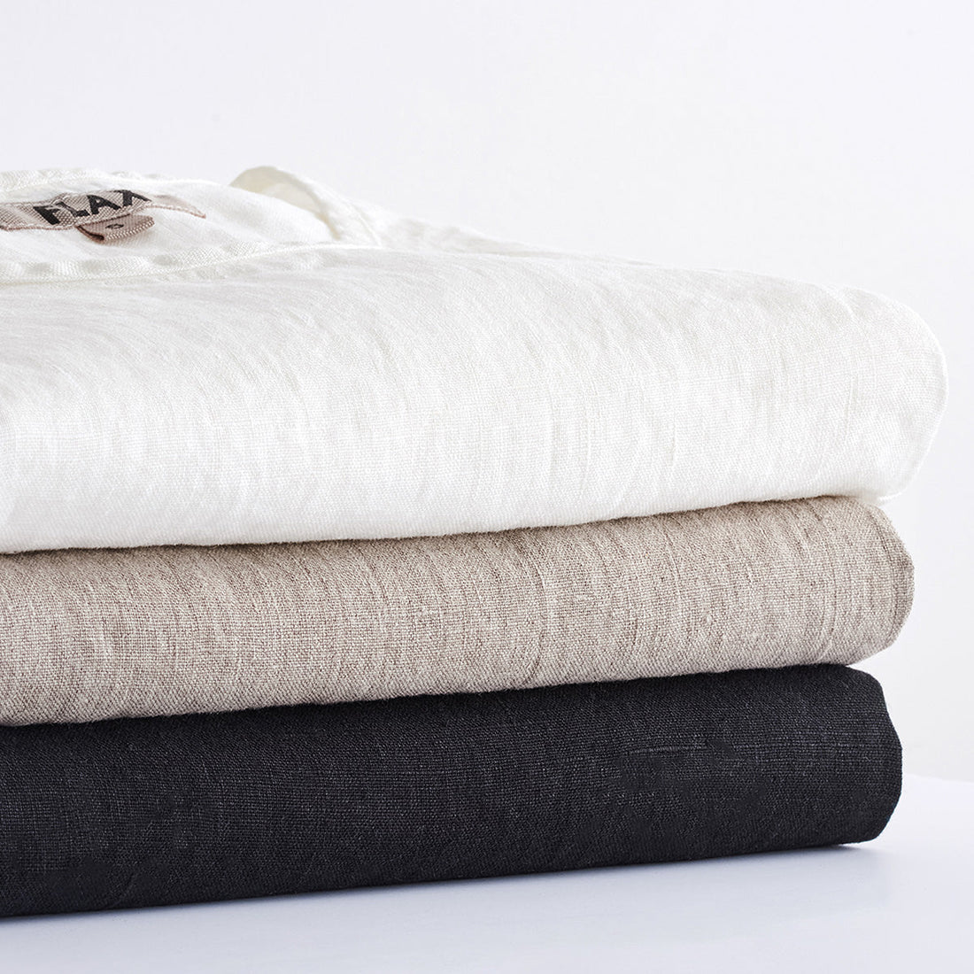 stacked linen shirts in white, natural, and black