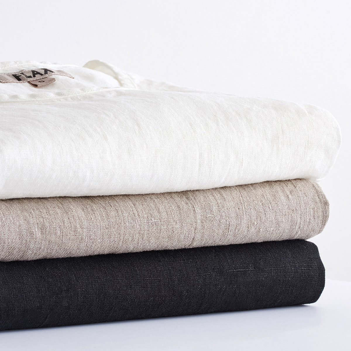 stacked linen shirts in white, natural, and black