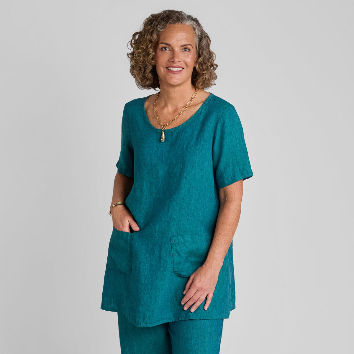 Woman in a blue short sleeve linen tunic with a hand in the pocket