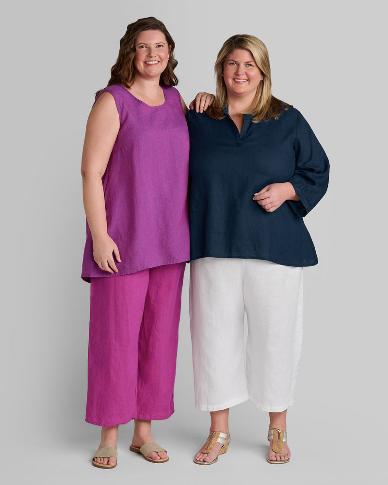 One woman in a purple linen tank and pink linen pants and another woman in a blue linen shirt and white linen pants