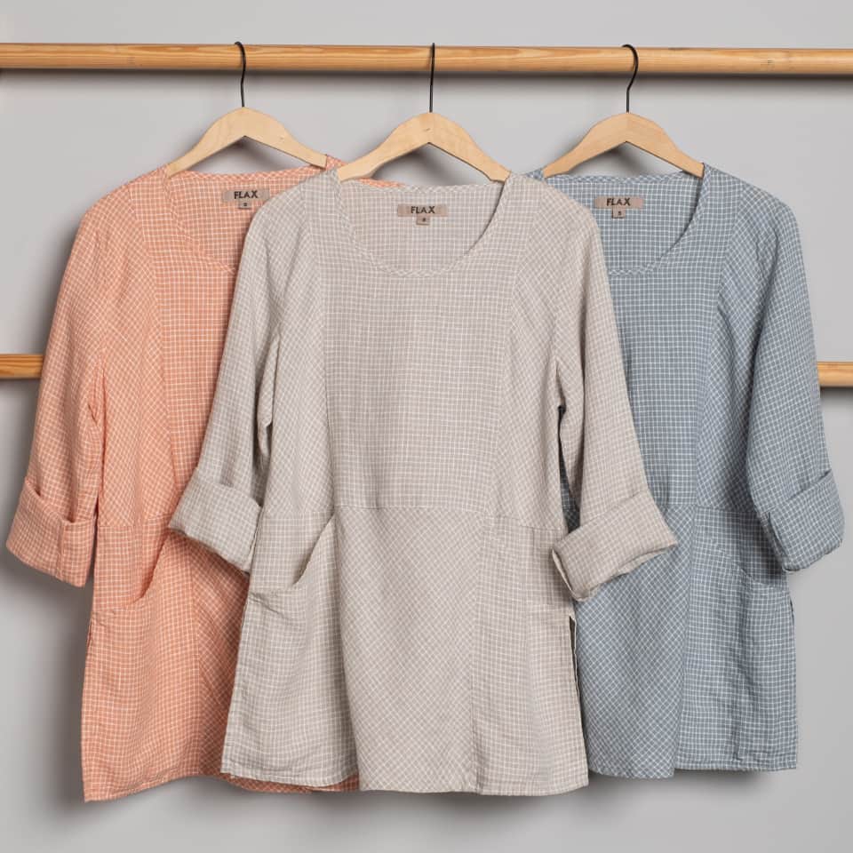 Three linen tunics with pockets in orange, beige, and blue on hangers