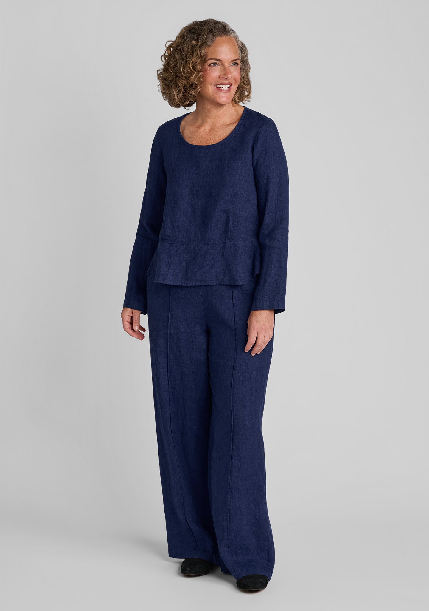 a woman modeling a matching navy blue two-piece linen set consisting of a long-sleeve peplum top and wide-leg trousers