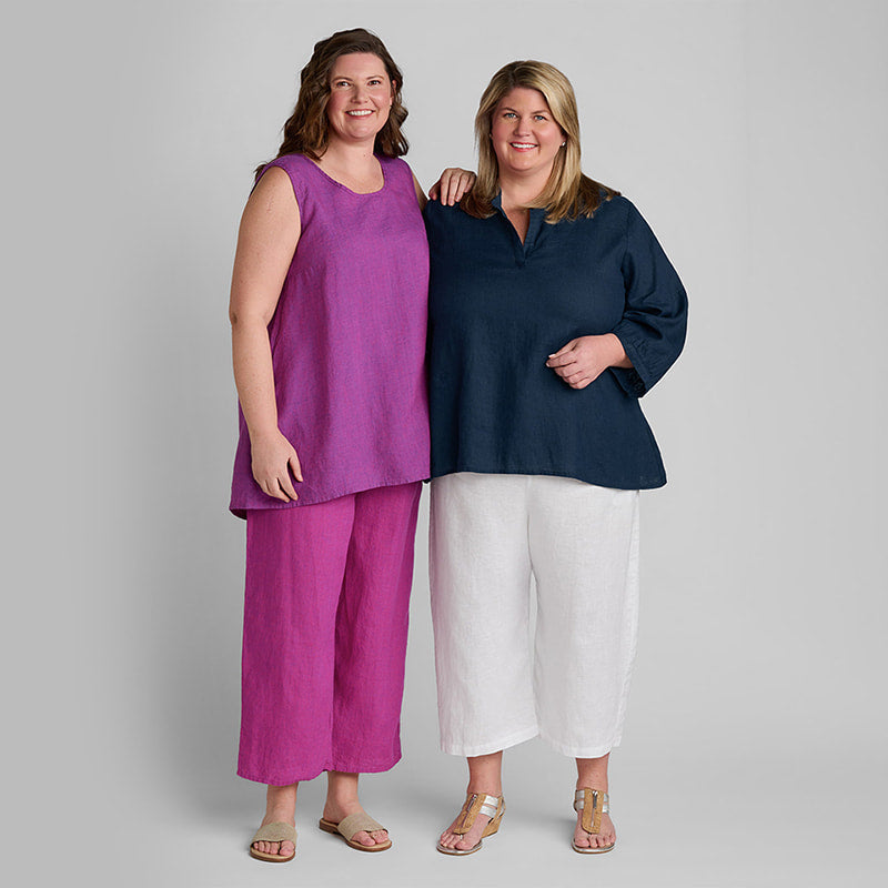 One woman in a purple and pink linen outfit and another woman in a blue linen shirt and white linen pants