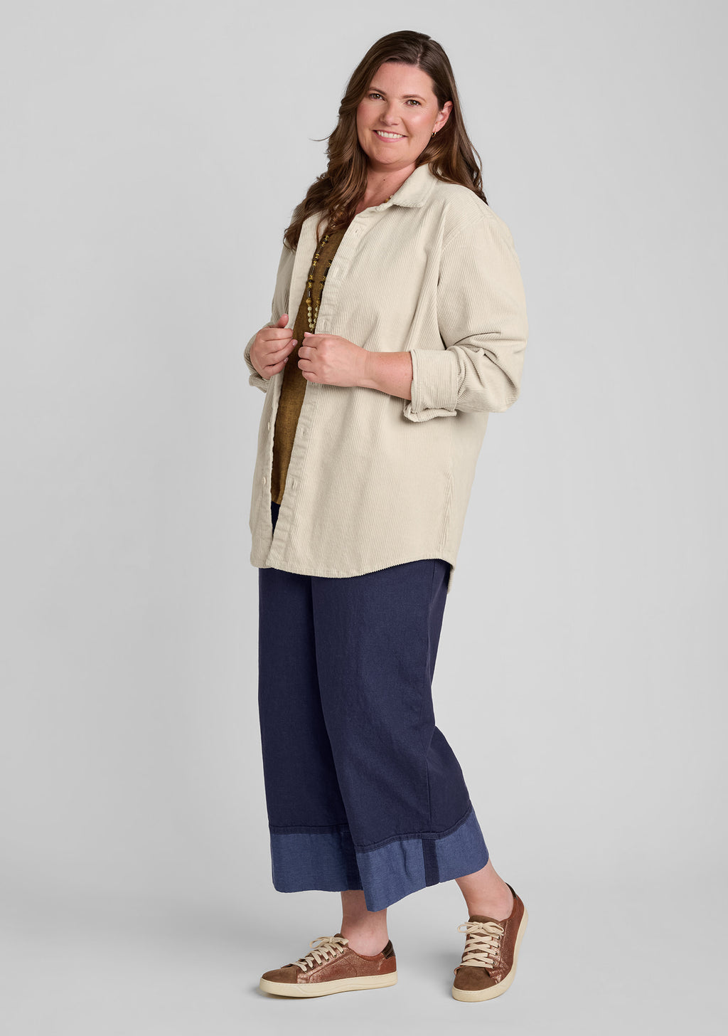 a woman modeling a light beige button-up shirt with rolled sleeves, paired with navy cropped denim pants