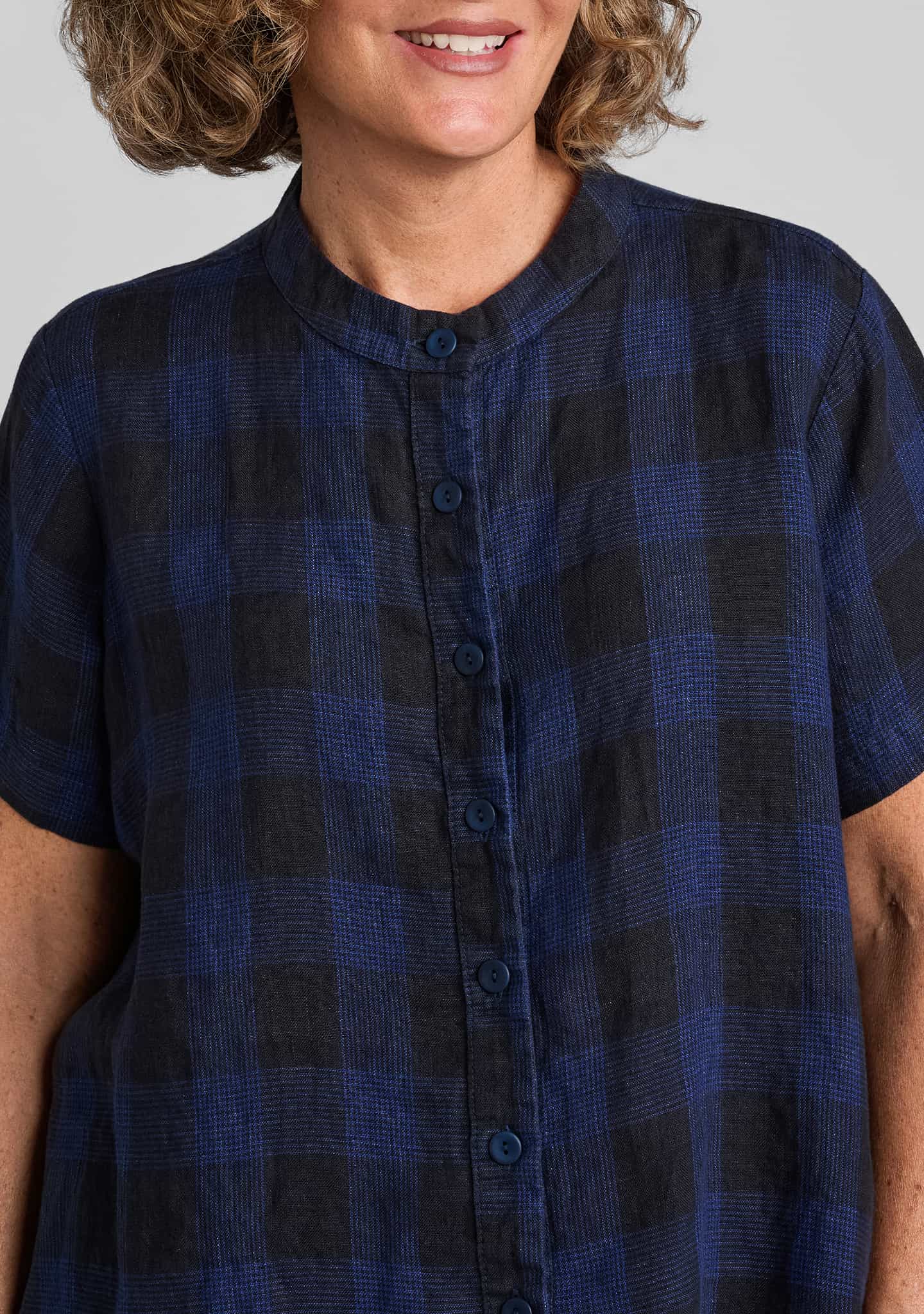 a close-up of a person wearing a short-sleeve button-front top with a dark blue and black plaid pattern